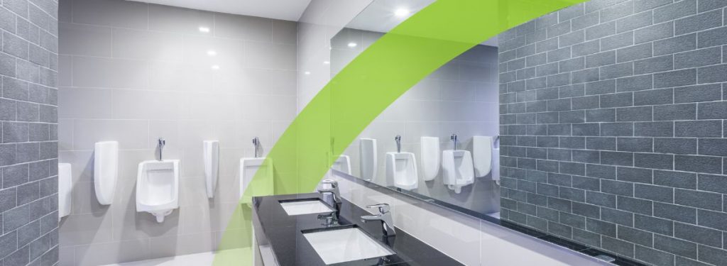 A clean, modern commercial public restroom featuring a black granite vanity with white basins, chrome faucets, and urinals against a grey tiled wall. A lime green brand swoosh overlays the image, representing Initial's professional hygiene services.